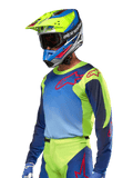 Alpinestars 2024 Racer Hoen Jersey, motorcross jersey, fluogeel en Blue Night Navy met rode logo's, gedragen met een bijpassende gele, blauwe en rode helm en blauwe handschoenen, opvallende uitrusting voor off-road racen