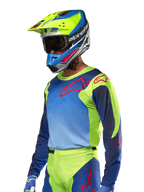 Alpinestars 2024 Racer Hoen Jersey, motorcross jersey, fluogeel en Blue Night Navy met rode logo's, gedragen met een bijpassende gele, blauwe en rode helm en blauwe handschoenen, opvallende uitrusting voor off-road racen