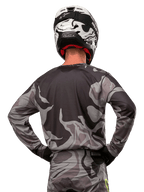 Alpinestars 2024 Racer Tactical Jersey, motorcross shirt, Cast Gray Camo Magnet, achteraanzicht met grijs en zwart camouflagepatroon, gedragen met bijpassende broek en een zwart-witte helm, professionele off-road race-uitrusting