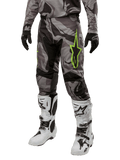Alpinestars 2024 Racer Tactical broek, motorcrossbroek, grijs en zwart camouflagepatroon, limoengroen sterlogo, gedragen met witte en zwarte laarzen en zwarte handschoenen, off-road motoruitrusting