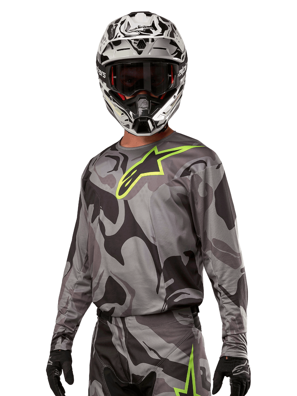 Alpinestars 2024 Racer Tactical Jersey, motorcross shirt, grijs camouflagepatroon met neon groen logo, gedragen met zwart-witte helm en zwarte handschoenen, technische vochtafvoerende stof voor off-road racing