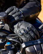 Alpinestars SP X 7 handschoenen, zwarte geperforeerde leren motorhandschoenen met TPU-knokkelbeschermers en vinger-sliders, afgebeeld op de handen van een motorrijder die een motorstuur vasthoudt