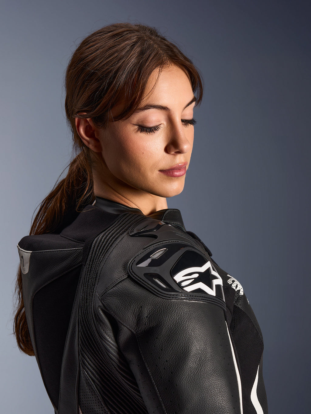 Vrouw die het Alpinestars Stella GP-R7 2-delig lederen pak draagt, close-up van de zwarte lederen schouder met DFS RR-bescherming en wit ster-logo, voorzien van de geïntegreerde aero-bult en geperforeerde details.