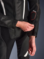 Close-up van het Alpinestars Stella GP-R7 2-delig leren pak in het zwart, met focus op de ritssluiting aan de onderarm, geperforeerde leren constructie, witte accenten en Tech-Air compatibele branding op de mouw.