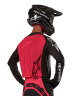 Alpinestars 2024 Supertech Ward Jersey, motorcross shirt, zwart en Red Berry, achterkant met rood mesh paneel en zwarte mouwen met witte logo's, gedragen met een zwarte carbon helm en handschoenen, atletische racepasvorm voor off-road rijden