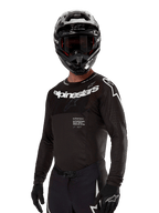 Alpinestars 2024 Supertech Ward Jersey, motorcross shirt, zwart en wit, performance-kleding met lange mouwen en opvallende Alpinestars-branding, gedragen met bijpassende helm en handschoenen, atletische pasvorm voor off-road rijden