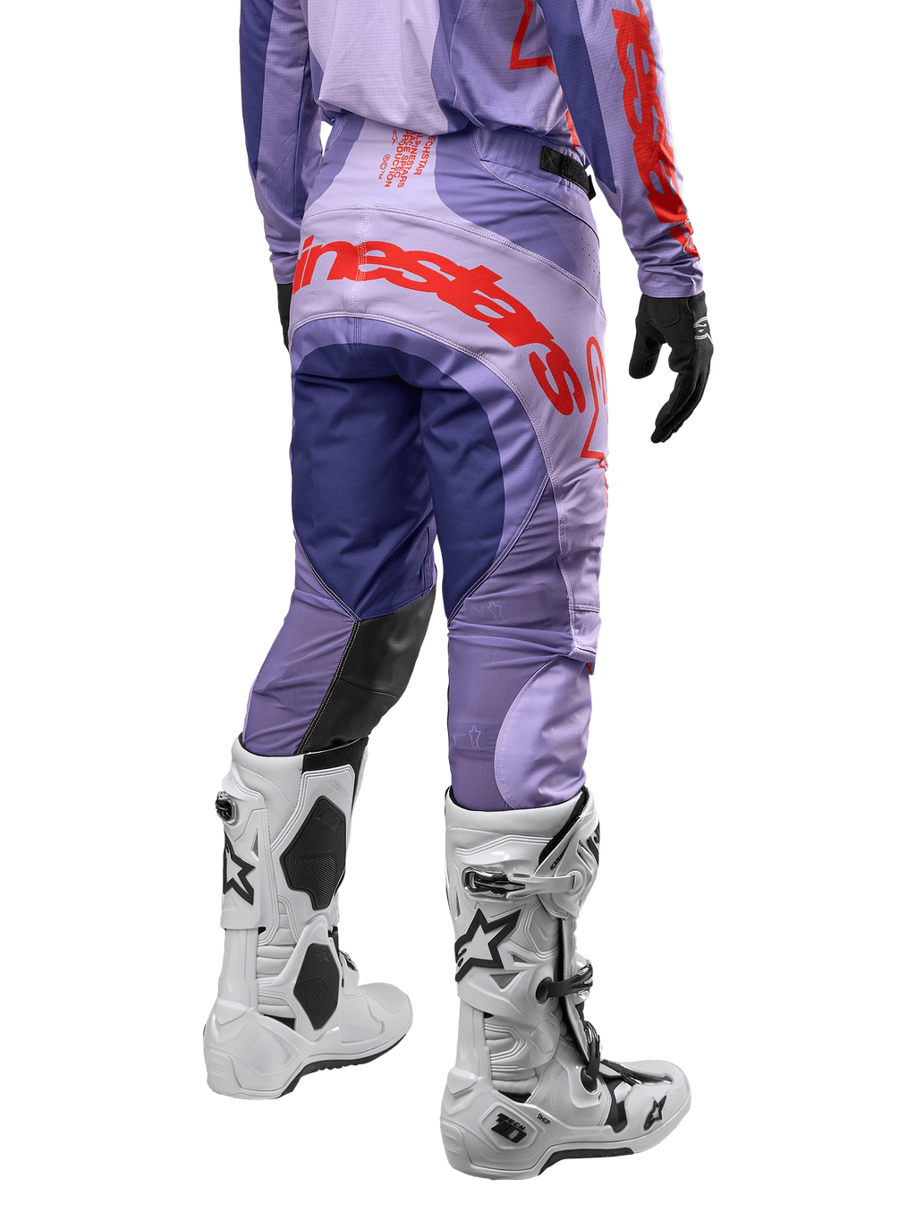 Alpinestars 2024 Techstar Ocuri crossbroek, motorcross broek, paars met feloranje accenten en grote logo-opdruk op het zitvlak, achteraanzicht, gedragen met witte motorcrosslaarzen en zwarte handschoenen