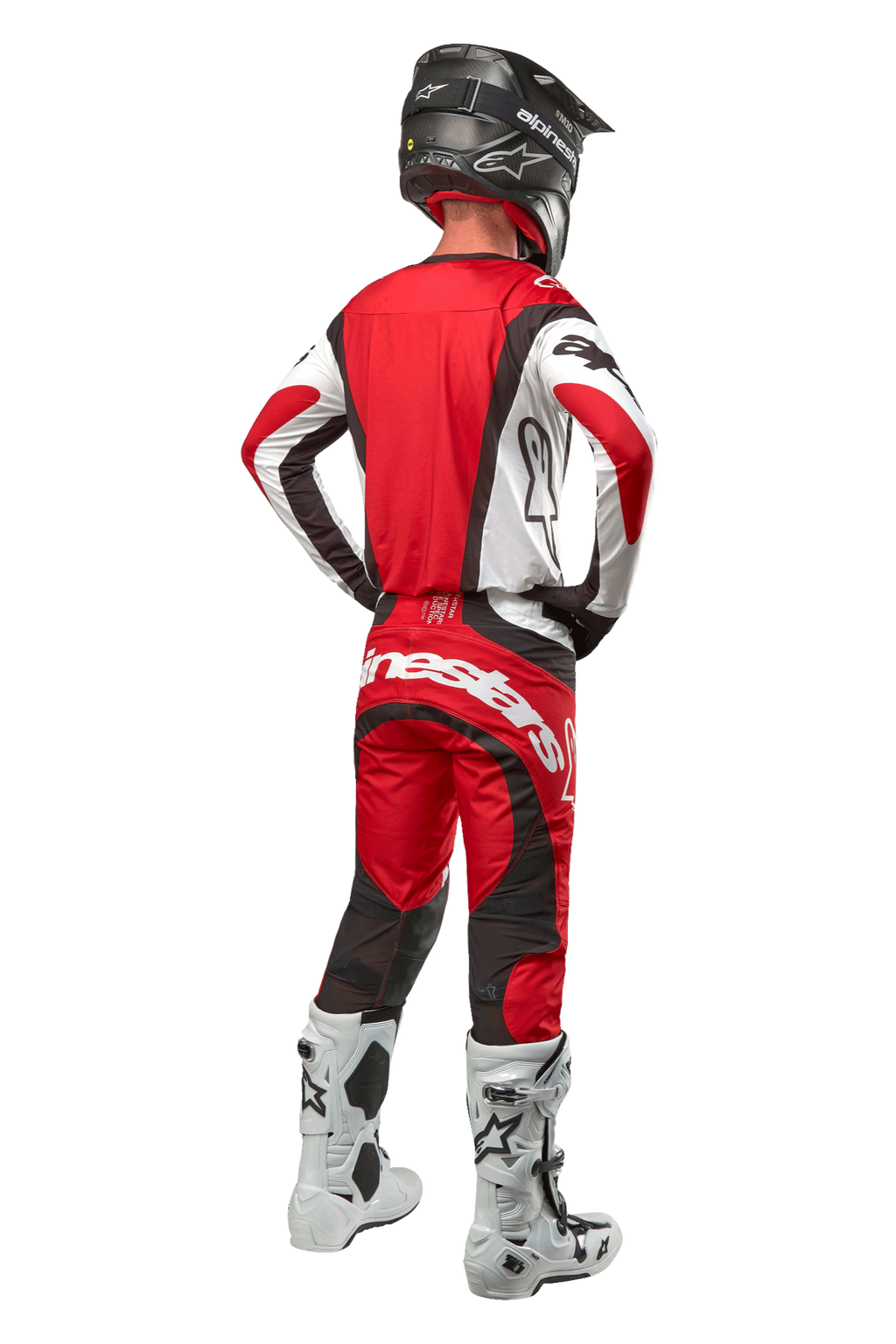 Alpinestars 2024 Techstar Ocuri broek, motorcrossbroek, Mars rood wit zwart, achteraanzicht van een motorcrosser in volledige race-uitrusting, inclusief bijpassende jersey, zwarte helm en wit-zwarte laarzen, met de nadruk op de Alpinestars-branding en duurzame materiaalconstructie.