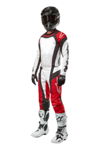 Motorcrosser in volledige Alpinestars uitrusting, 2024 Techstar Ocuri Pants in Mars Red White Black, bijpassend shirt, zwarte helm met crossbril, zwart-witte handschoenen en witte motorcrosslaarzen, professionele off-road race-outfit