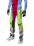 Alpinestars 2024 Techstar Ocuri crossbroek, motorcross broek, lichtblauw, bessenrood en neongeel, gedragen met bijpassende uitrusting en witte laarzen, voorzien van opvallende Astars-branding en een prestatiegerichte racepasvorm.