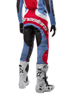 Alpinestars 2024 Techstar Ocuri broek, motorcrossbroek, lichtblauw, marsrood en wit, achteraanzicht met de nadruk op het grote rode Alpinestars-logo op het zitvlak, gedragen met witte motorcrosslaarzen en bijpassende jersey.