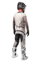 Alpinestars 2024 Techstar Pneuma broek, motocrossbroek, Dark Sand en Iron Dust Gray, achteraanzicht gedragen door een rijder met een bijpassende jersey, witte en zwarte laarzen en een zwarte helm, voorzien van opvallende Alpinestars-branding op het zitvlak en versterkte donkere panelen