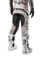Alpinestars 2024 Techstar Pneuma crossbroek, motorcross broek, Dark Sand en Iron Dust Gray, achteraanzicht vanaf de taille naar beneden, opvallende zwarte Alpinestars-branding op het zitvlak, gedragen met wit-zwarte motorcrosslaarzen en zwarte handschoenen, duurzaam race-fit ontwerp voor off-road competitie