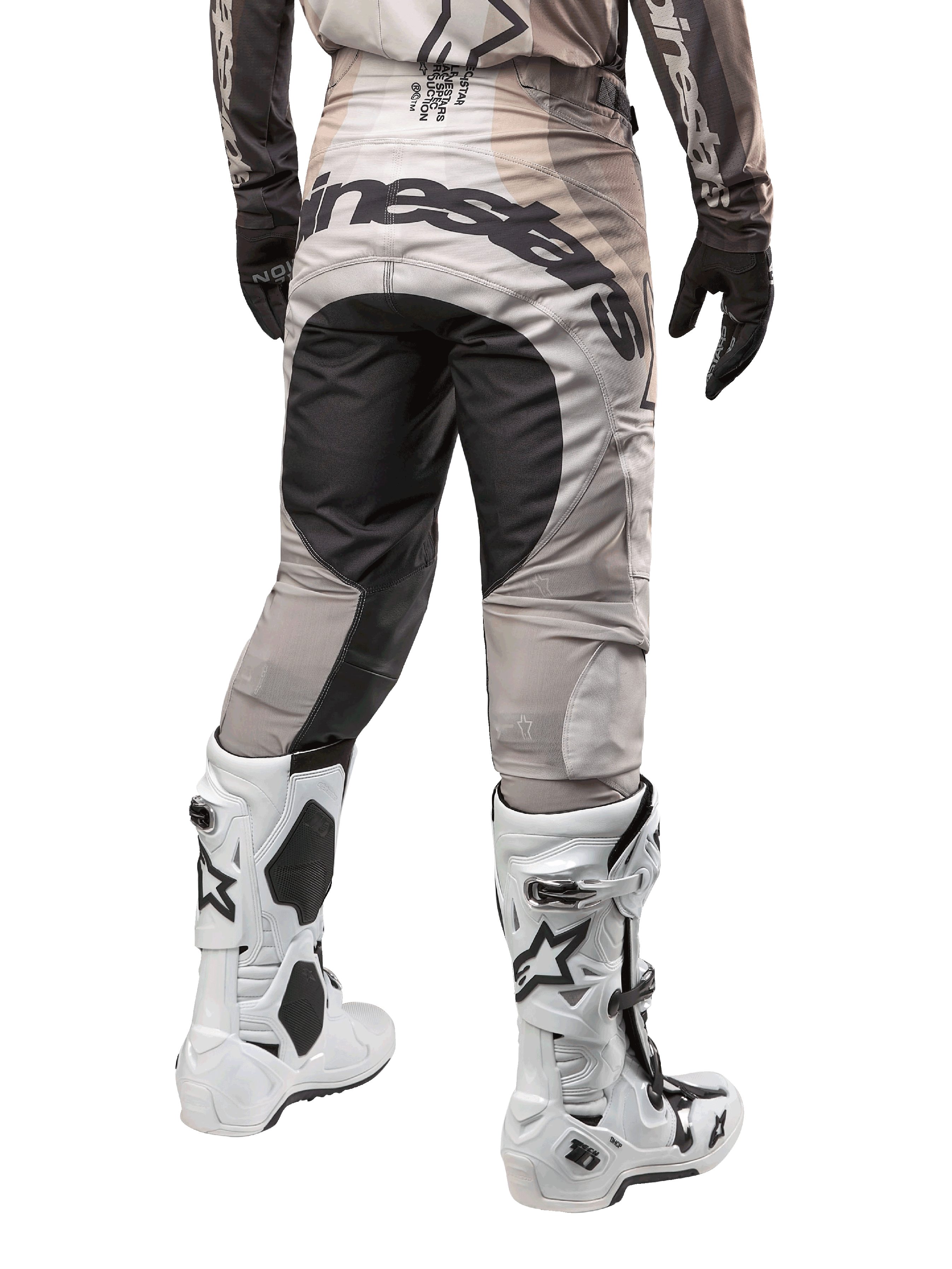 Alpinestars 2024 Techstar Pneuma crossbroek, motorcross broek, Dark Sand en Iron Dust Gray, achteraanzicht vanaf de taille naar beneden, opvallende zwarte Alpinestars-branding op het zitvlak, gedragen met wit-zwarte motorcrosslaarzen en zwarte handschoenen, duurzaam race-fit ontwerp voor off-road competitie