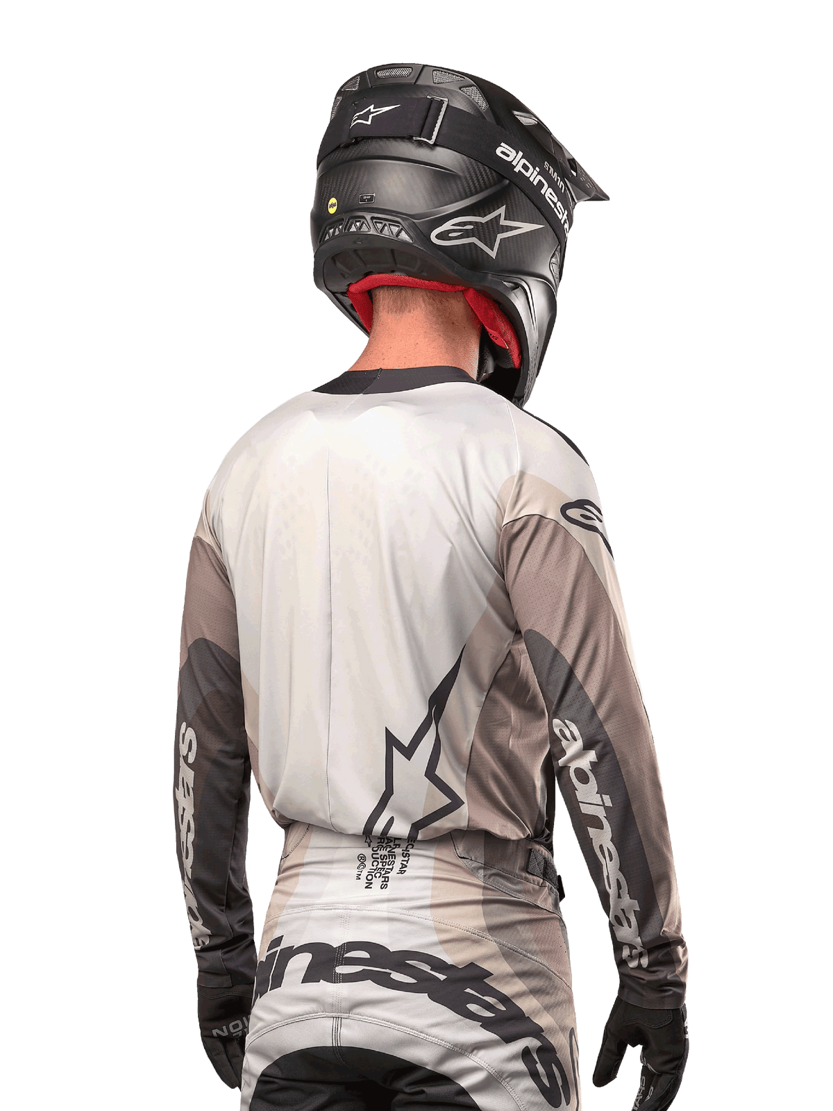 Alpinestars 2024 Techstar Pneuma Jersey, motocross shirt rugaanzicht, kleur Dark Sand Iron Dust Gray, zwarte helm met carbon-afwerking, groot sterlogo op de rug en Alpinestars-branding op de mouwen