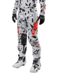 Alpinestars 2024 Techstar Rantera crossbroek, motorcross broek, Haze Gray Camo met zwart en rood abstract patroon, gedragen met bijpassende jersey, zwarte handschoenen en witte motorcrosslaarzen, ontworpen voor high-performance off-road racen