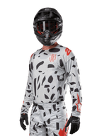 Alpinestars 2024 Techstar Rantera Jersey, motorcross shirt, Haze Gray Camo met zwarte abstracte patronen en rode accenten, ontwerp met lange mouwen gedragen met bijpassende zwarte helm en handschoenen, technische off-road race-uitrusting