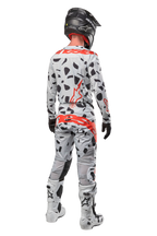 Motorcrosser van achteren in Alpinestars 2024 Techstar Rantera Pants, Haze Gray Camo met zwarte vlekken en rode logo's, bijpassende jersey, zwarte helm en witte laarzen, complete off-road race-outfit