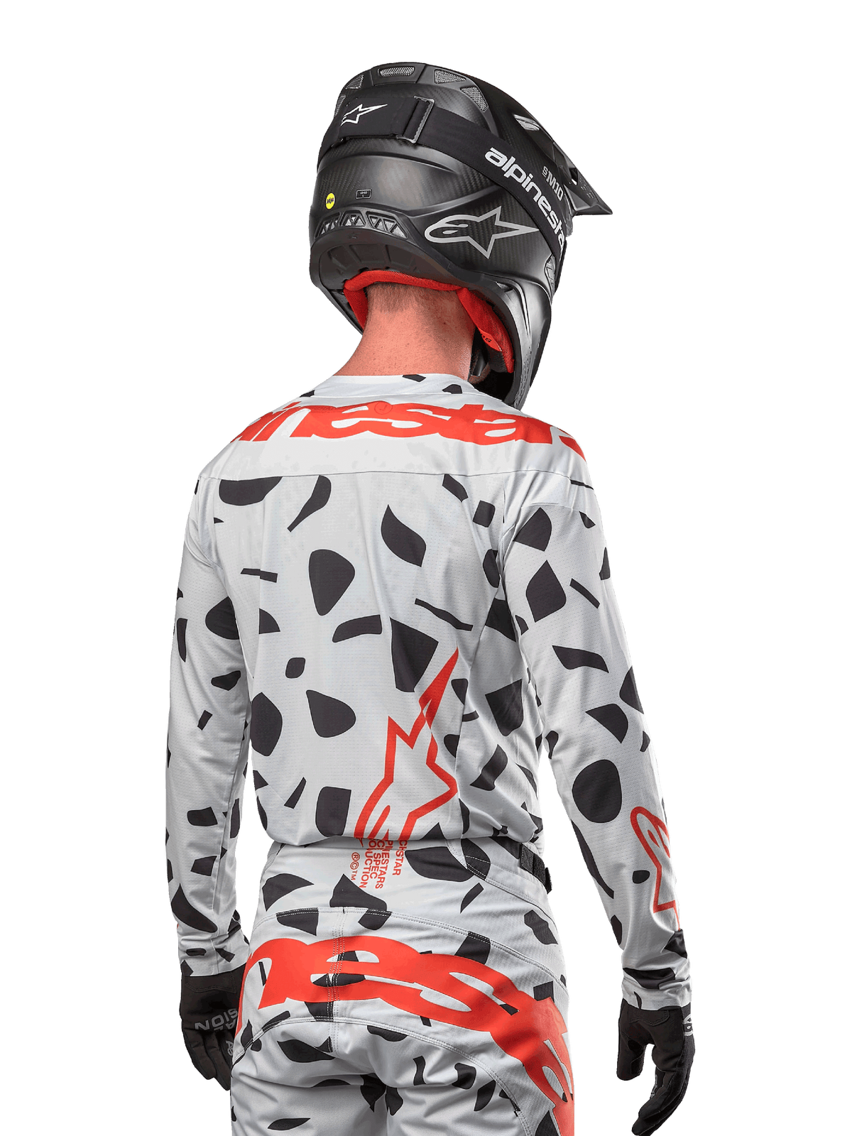 Motorcrosser vanaf de achterkant gezien, gekleed in de Alpinestars 2024 Techstar Rantera Jersey in Haze Gray Camo, met een lichtgrijze basis met zwarte grafische vlekken en opvallende rode Alpinestars-logo's op de rug en schouders, gecombineerd met een bijpassende broek en een zwarte helm.
