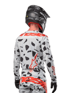 Motorcrosser vanaf de achterkant gezien, gekleed in de Alpinestars 2024 Techstar Rantera Jersey in Haze Gray Camo, met een lichtgrijze basis met zwarte grafische vlekken en opvallende rode Alpinestars-logo's op de rug en schouders, gecombineerd met een bijpassende broek en een zwarte helm.