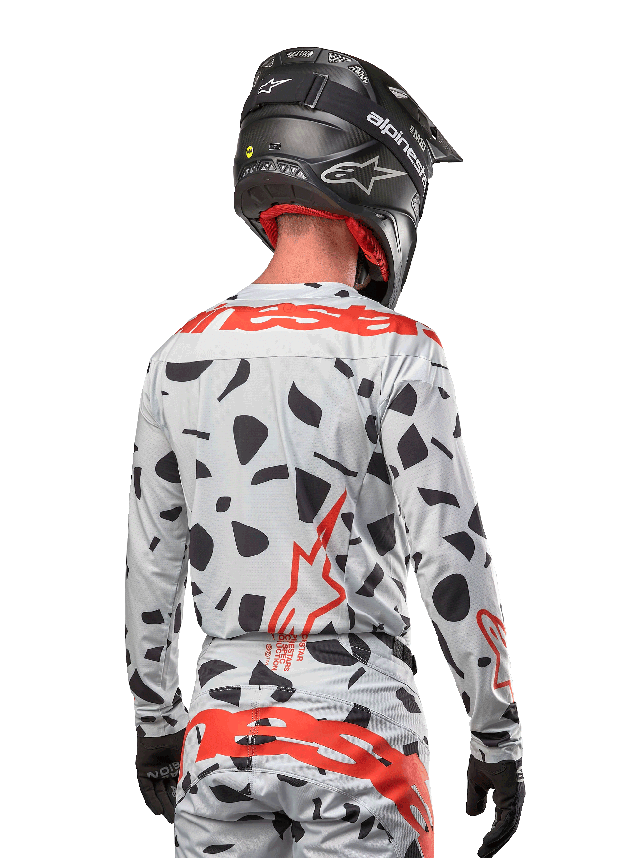 Motorcrosser vanaf de achterkant gezien, gekleed in de Alpinestars 2024 Techstar Rantera Jersey in Haze Gray Camo, met een lichtgrijze basis met zwarte grafische vlekken en opvallende rode Alpinestars-logo's op de rug en schouders, gecombineerd met een bijpassende broek en een zwarte helm.