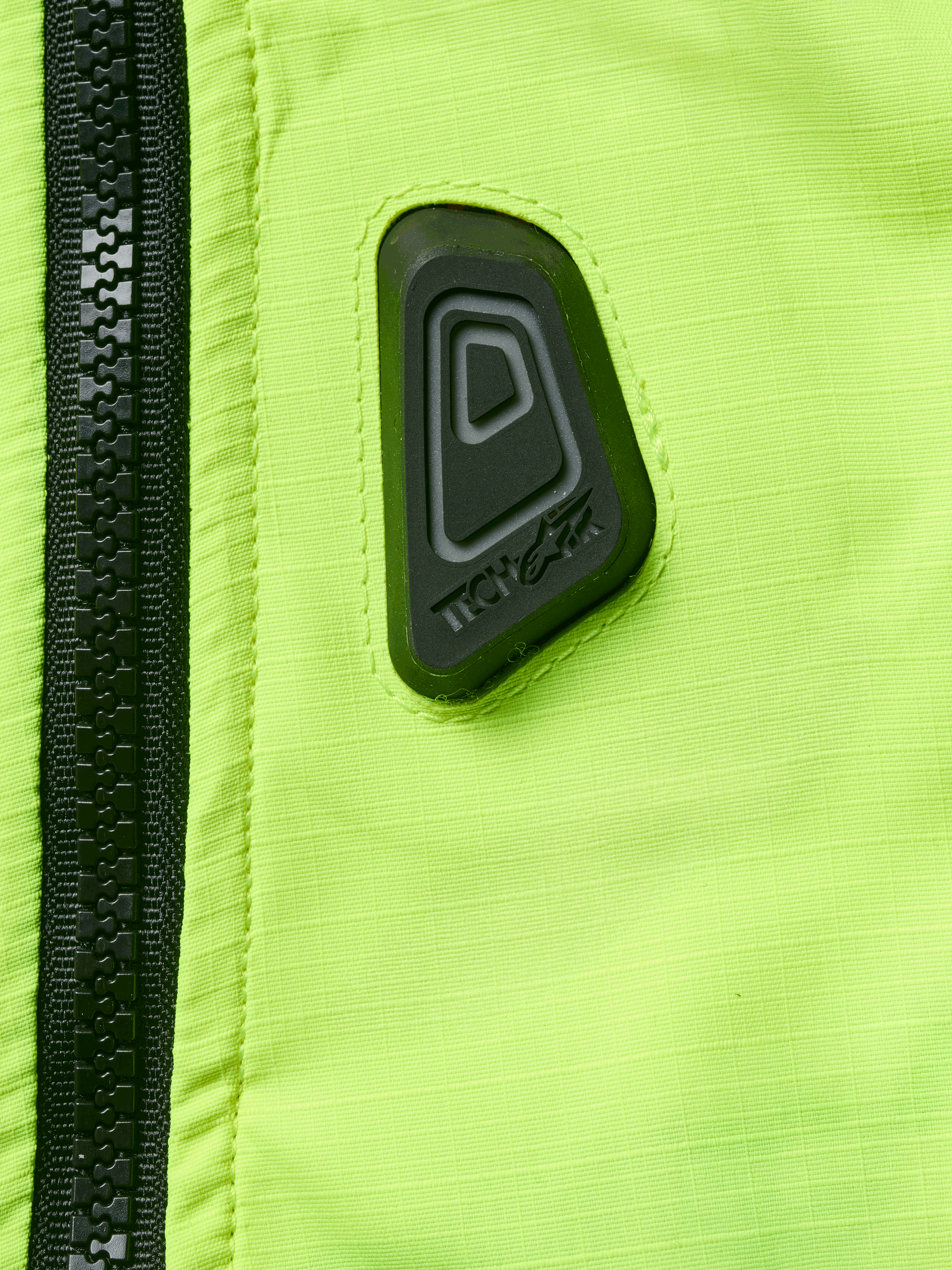 Alpinestars Tech-Air® 3 V2 Systeem, motor airbagvest, close-up van Yellow Fluo waterbestendige stof met zwarte rits, voorzien van een zwarte rubberen Tech-Air logopatch, high-visibility veiligheidsuitrusting