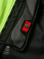 Alpinestars Tech-Air® 3 V2 Systeem detail, close-up van intern meshvak met rood treklipje en druksluiting, opvallend geel fluo paneel, zwarte textiele constructie met airbagmodule-label en rits