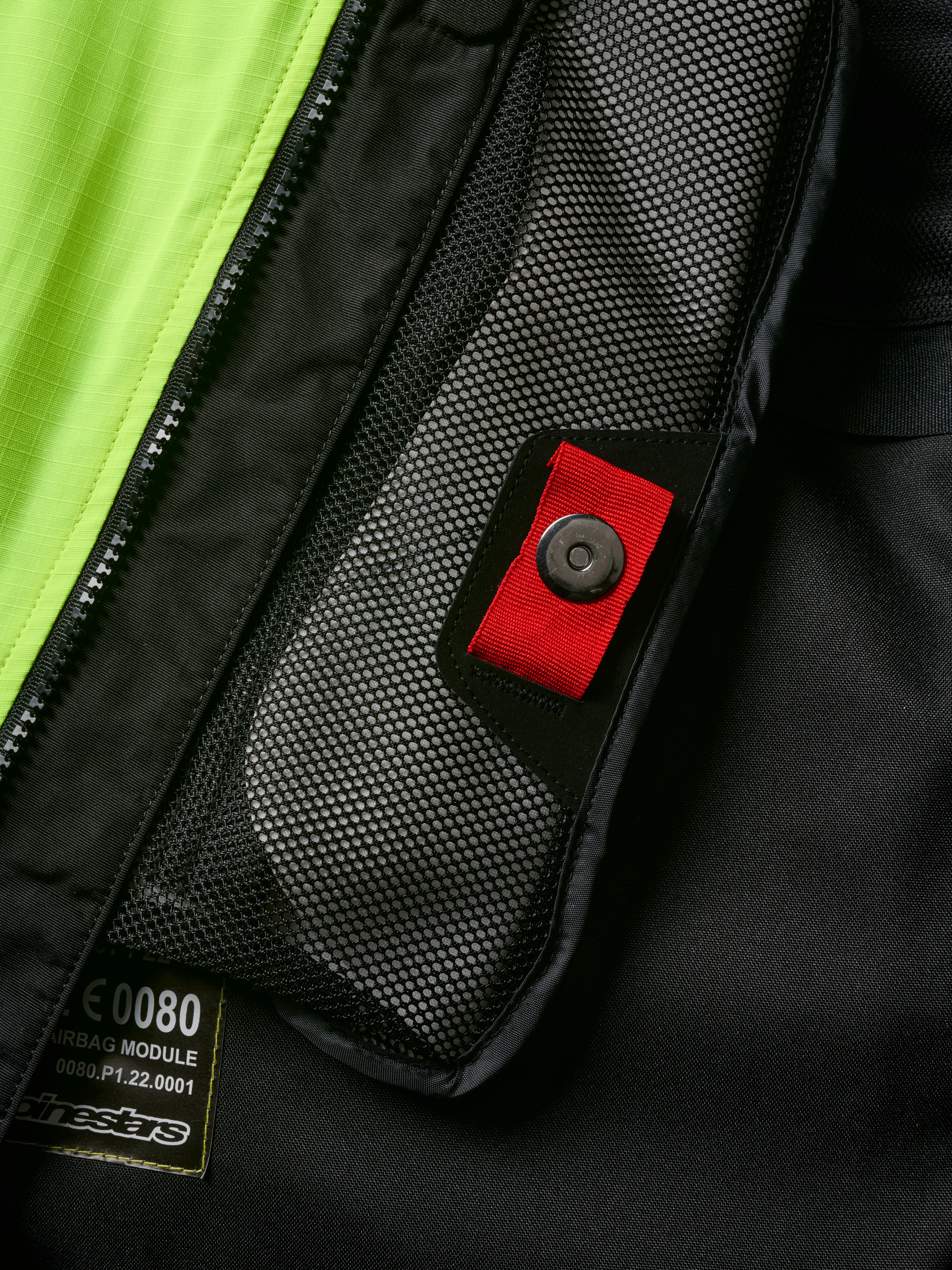 Alpinestars Tech-Air® 3 V2 Systeem detail, close-up van intern meshvak met rood treklipje en druksluiting, opvallend geel fluo paneel, zwarte textiele constructie met airbagmodule-label en rits