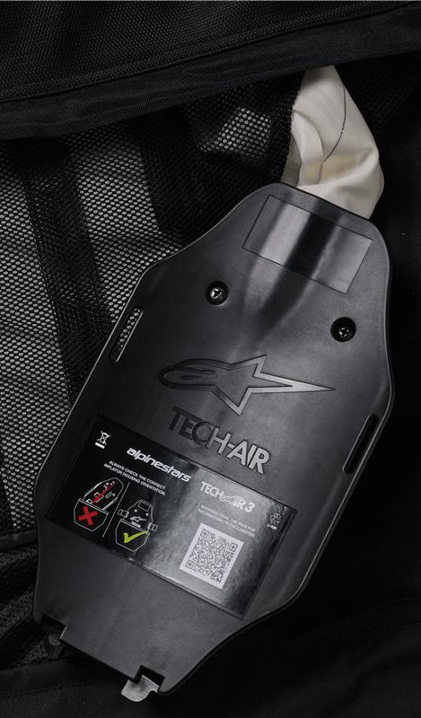 Alpinestars Tech-Air 3 V2 Systeem, binnenaanzicht van de gasinflator en ECU-behuizing, zwart kunststof met reliëflogo, veiligheidslabel met QR-code en installatiediagrammen, zwarte mesh binnenvoering, detail van het door de gebruiker te onderhouden autonome airbagsysteem