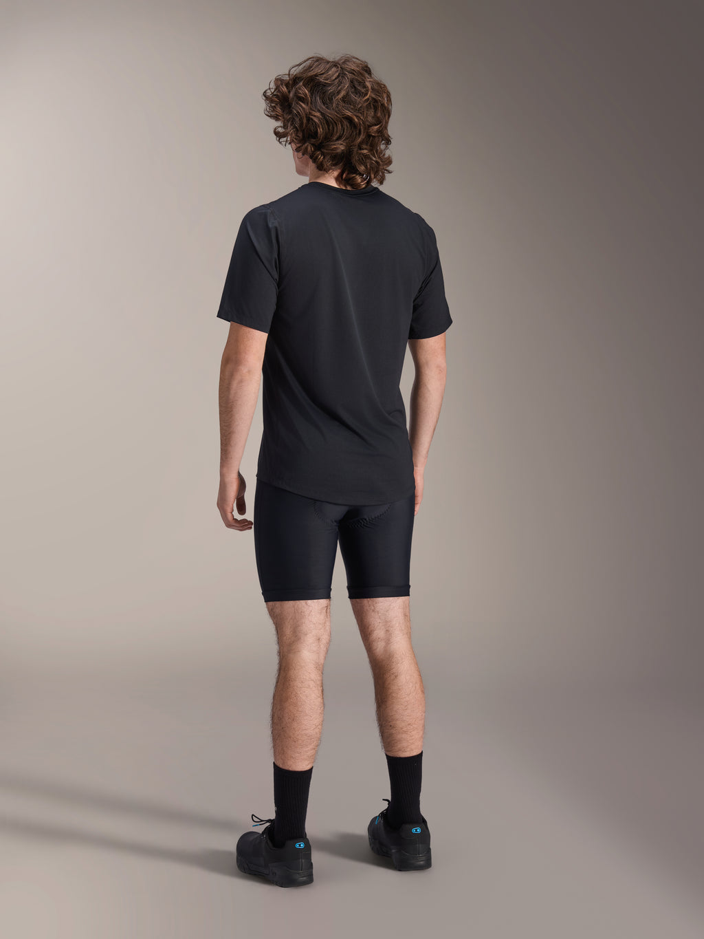 Alpinestars A-Dura Liner Shorts, zwarte fiets-linershorts, achteraanzicht op model, nauwsluitende stretchstof met zichtbare naden van de zeemvulling, gecombineerd met een zwart t-shirt en fietsschoenen, mountainbikekleding