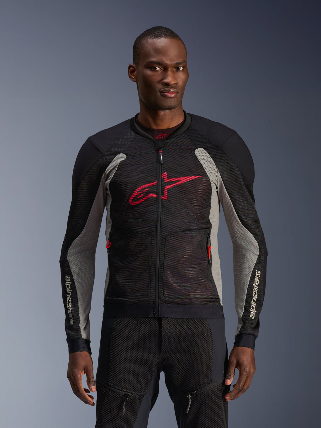 Alpinestars Troop-Air Jacket, motorjas met mesh panelen, zwart en asgrijs met felrode accenten, gedragen door een model, voorzien van ademende 2D tech mesh-panelen voor ventilatie, een groot rood Astars-logo op de borst en een technisch sportief ontwerp voor stadsritten