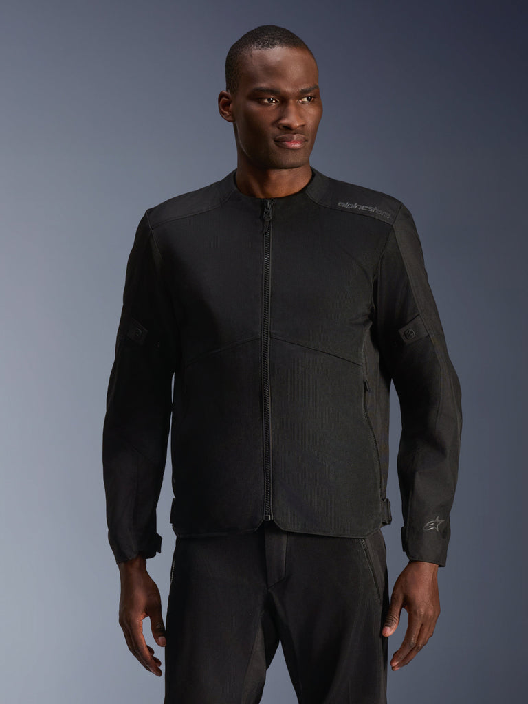 Mannelijk model draagt Alpinestars C-1 Air Jacket in het zwart, eigentijdse motorjas met uitgebreide tech mesh-panelen en een volledige ritssluiting aan de voorzijde, gecombineerd met bijpassende zwarte motorbroek, urban lifestyle en woon-werkverkeer uitstraling