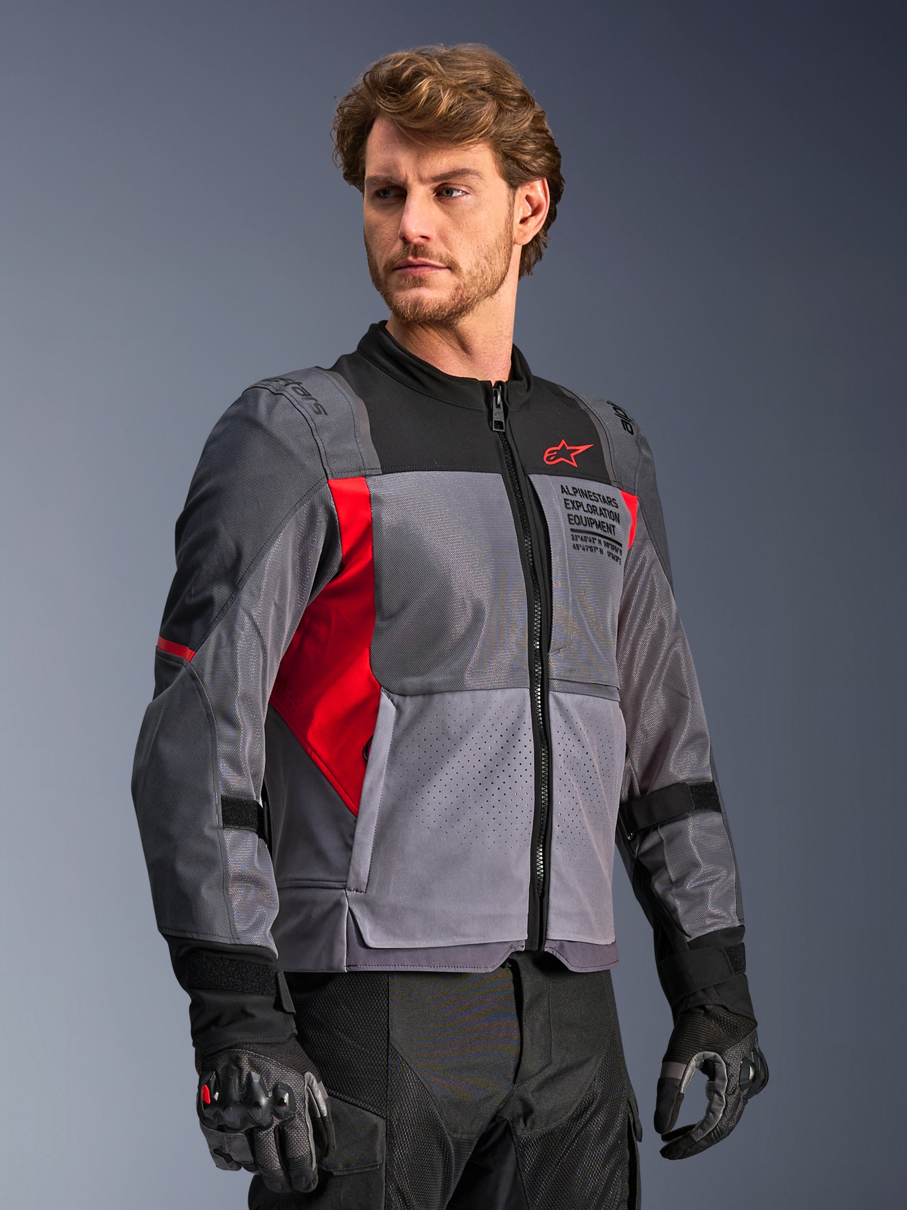 Alpinestars St-2 Air Jacket, motorjas, diepgrijs en donkergrijs met felrode accenten, voorzien van grote mesh-ventilatiepanelen, lasergeperforeerde details en rood sterlogo, gedragen door een model in een studio-omgeving, moderne adventure touring-stijl