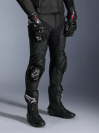 Missile V3 Leren Broek, zwarte motorracebroek, gedragen met bijpassende GP Pro-handschoenen en technische racelaarzen, premium lederen constructie met witte logo-knieschuivers, professionele race-esthetiek voor circuit- en weggebruik