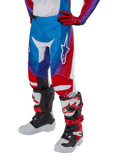Alpinestars Youth 2024 Racer Pneuma motorcrossbroek, crossbroek, blauw, rood en wit, gedragen met bijpassende handschoenen en laarzen, voorzien van een wit sterlogo op de dij, sportief ontwerp voor off-road rijden
