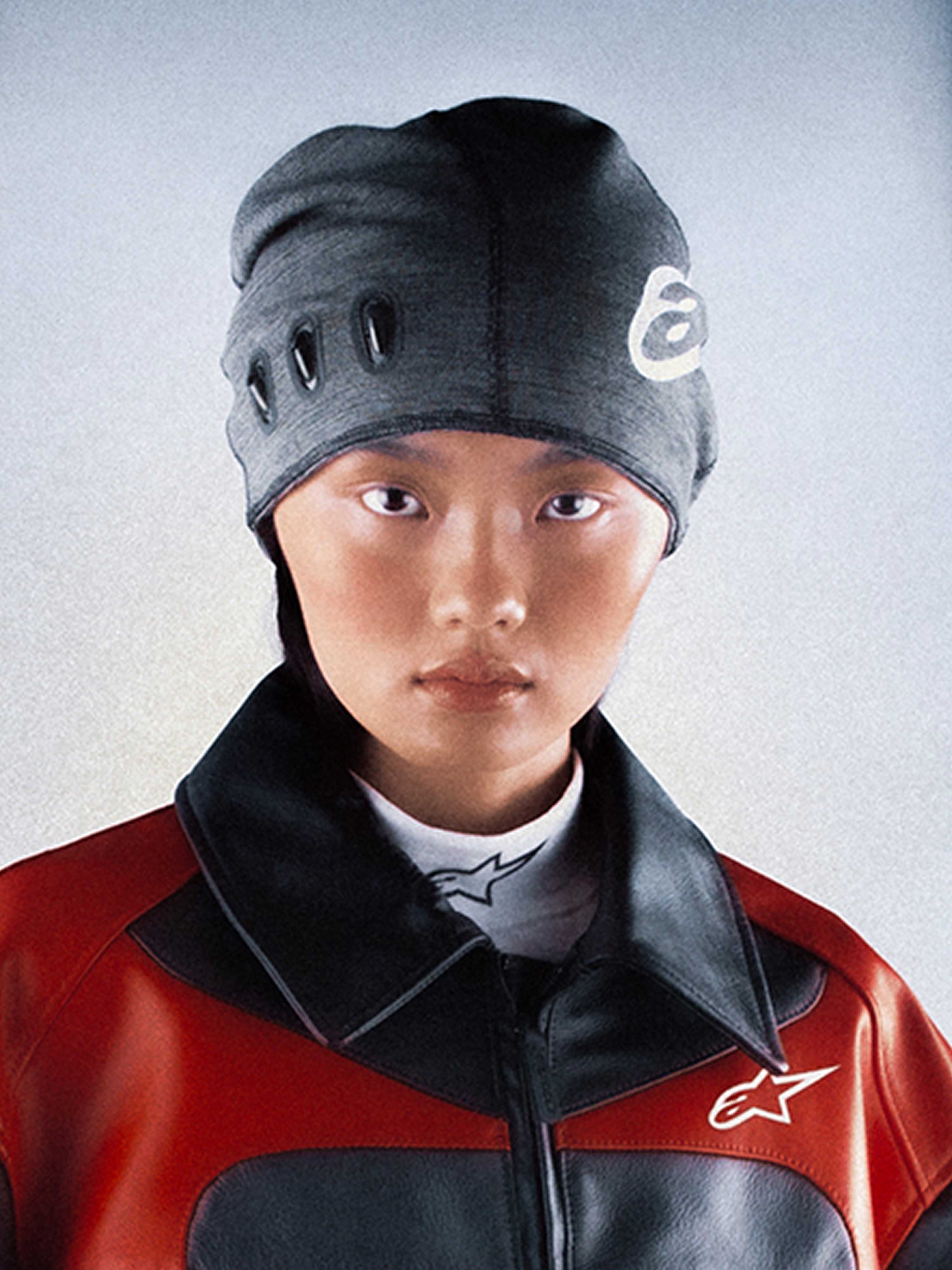Alpinestars RSRV Onyx beanie, premium gebreide muts, donkergrijs met wit logo, ovale uitsnedes, unisex streetwear accessoire, gedragen met rood-zwarte jas
