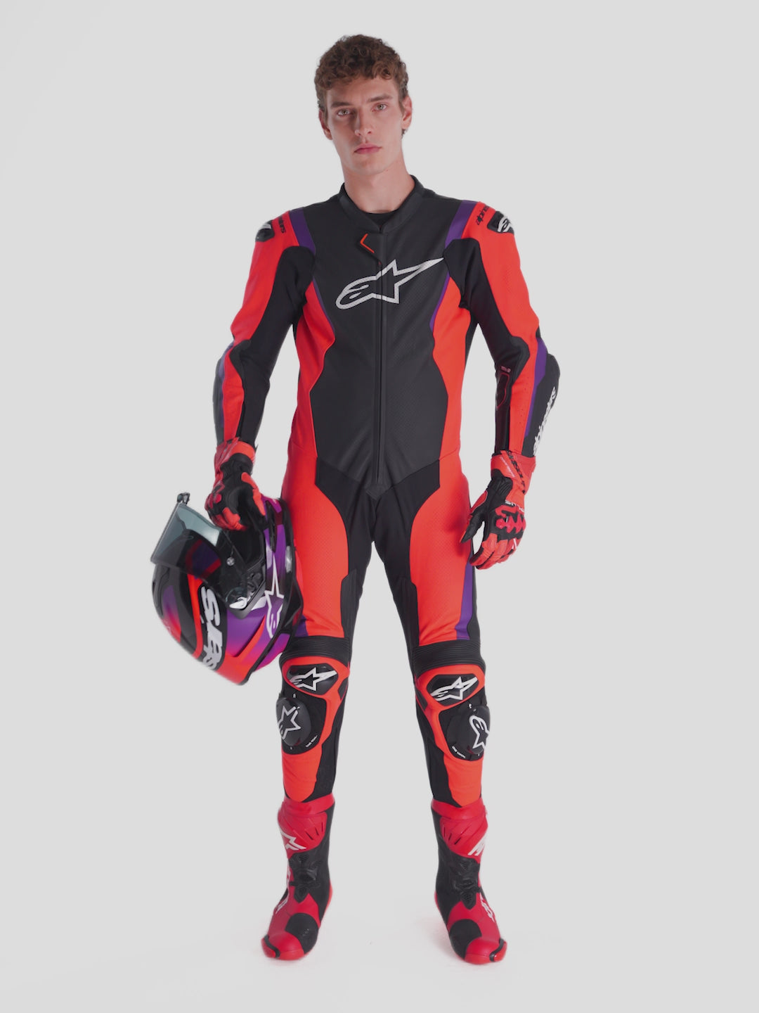 Alpinestars Missile V3 Leather Suit - 1 Piece, men's one-piece motorcycle racing suit in black, red, and purple, worn by a model holding a helmet, showcasing AAA-rated leather construction and DFS armor